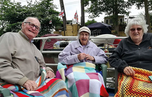 Three elderly people sat together under knitted blankets