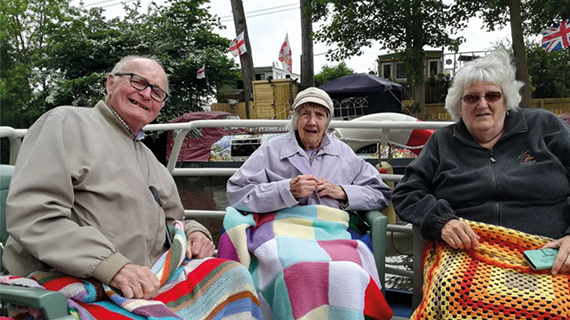 Three elderly people sat together under knitted blankets